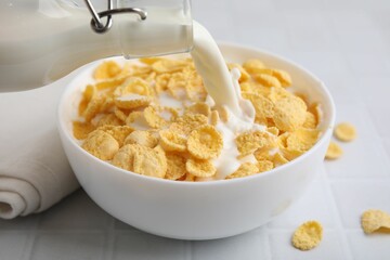 Breakfast cereal. Pouring milk into bowl with tasty corn flakes at white table, closeup