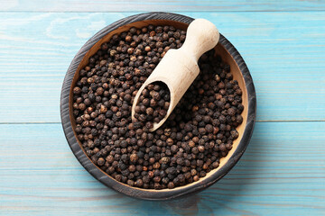 Aromatic spice. Black pepper in bowl and scoop on light blue wooden table, top view