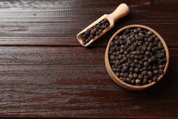 Aromatic spice. Black pepper in bowl and scoop on wooden table, top view. Space for text