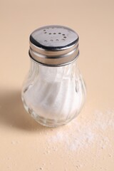 Natural salt in shaker on beige background, closeup