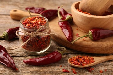 Chili pepper flakes and pods on wooden table, closeup