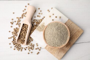 Aromatic spice. Ground pepper in bowl and scoop with peppercorns on white wooden table, flat lay