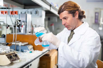 Fototapeta premium Adult man scientist in a medical gown conducts experiments with liquids in the laboratory