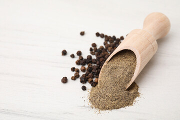 Aromatic spice. Ground pepper in scoop and black peppercorns on white wooden table, closeup. Space...