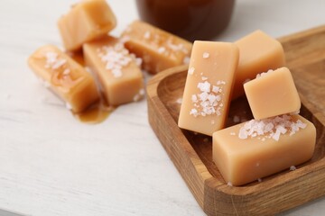 Yummy caramel candies, sauce and sea salt on white wooden table, closeup