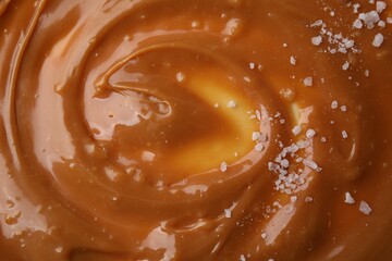 Delicious caramel sauce with sea salt as background, closeup