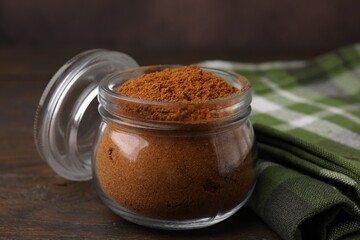 Ground red pepper in jar on wooden table, closeup
