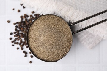 Ground pepper and peppercorns on white tiled table, top view