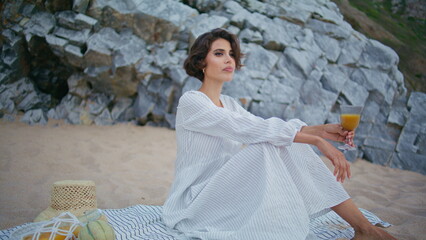 Elegant woman relaxing seaside picnic. Beautiful lady posing holding juice