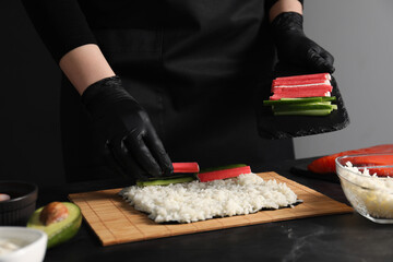 Chef in gloves making sushi roll at dark table, closeup
