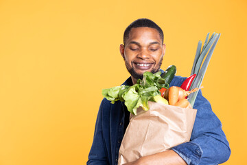 Positive enthusiastic guy smiling at his ethically sourced groceries, feeling pleased with his...