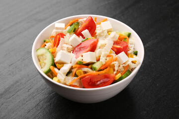 Tasty salad with Chinese cabbage, carrot, cheese, cucumber, corn and tomato on black table