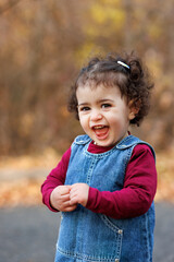 Cute laughing kid in overalls and red top stands still in a world of autumnal hues