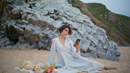 Attractive lady taking smartphone selfie on sandy shore. Romantic girl on picnic