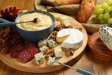 Fondue pot with tasty melted cheese, forks and different snacks on wooden table