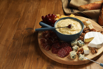 Fondue pot with tasty melted cheese, forks and different snacks on wooden table