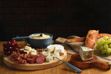 Fondue pot with tasty melted cheese, forks and different snacks on wooden table