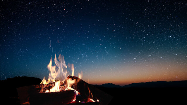 a bonfire burns at night against the background of mountains and sea with bright stars..