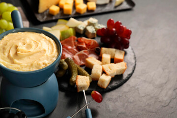 Fondue with tasty melted cheese, forks and different snacks on black table