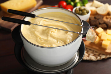 Fondue with tasty melted cheese, forks and piece of bread on table