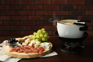 Fondue with tasty melted cheese, forks and different snacks on wooden table