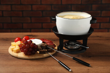 Fondue with tasty melted cheese, forks and different snacks on wooden table