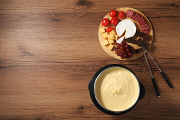 Fondue with tasty melted cheese, forks and different snacks on wooden table, top view. Space for...