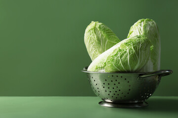 Fresh Chinese cabbages in colander on green background, closeup. Space for text