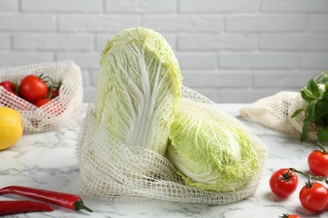 Fresh Chinese cabbages and other vegetables on white marble table near brick wall