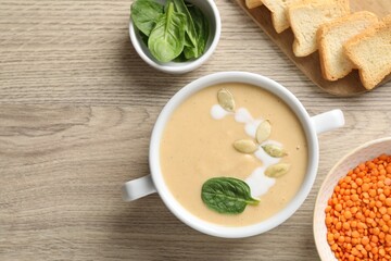 Healthy cream soup high in vegetable fats, bread and spinach on wooden table, flat lay. Space for text