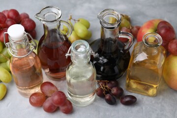 Different types of vinegar and fresh fruits on grey table