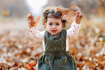 The joy of autumn. Playful little girl standing with leaves, amidst the season s painted leaves