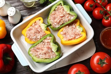 Raw stuffed peppers in dish and ingredients on wooden table, flat lay
