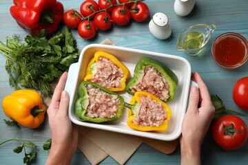 Woman holding dish with raw stuffed peppers at light blue wooden table, top view