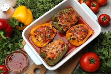Tasty stuffed peppers in dish and ingredients on grey table, above view