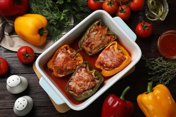 Tasty stuffed peppers in dish and ingredients on wooden table, flat lay