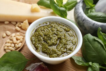 Tasty pesto sauce in bowl, basil, pine nuts and cheese on table, closeup