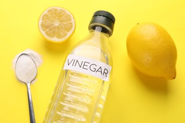 Eco friendly natural cleaners. Vinegar in bottle, lemons and spoon of soda on yellow background