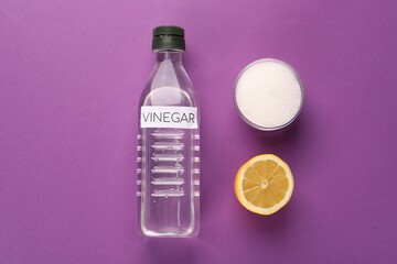 Eco friendly natural cleaners. Vinegar in bottle, cut lemon and bowl of soda on purple background, flat lay