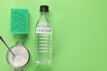 Eco friendly natural cleaners. Vinegar in bottle, sponge and jar of soda on green background, flat lay. Space for text
