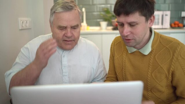 Senior man receiving computer lessons from adult son, bridging generation gap through technology education.