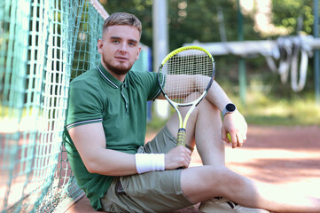 Young happy handsome man in polo play tennis outdoors with tennis racket on court at summer day