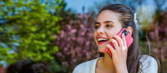 Young happy laughing woman talking on mobile phone isolated outdoors background. Cheerful woman is talking over the phone. Smiling girl talks on cellular telephone outdoors