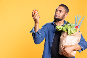 Vegan male person admiring a fresh ethically sourced tomato and smelling the fresh aroma in studio,...
