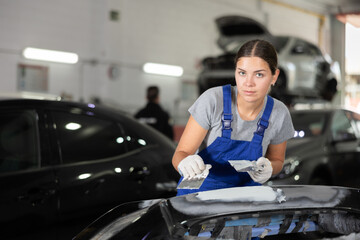 Female mechanic prepares car for painting in workshop - grinds and puts putty on the bumper before...