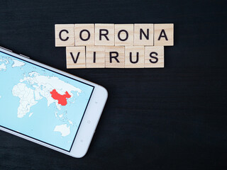 Coronavirus word made of wood block and world map on smartphone screen. Coronavirus text on...