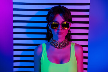 Portrait of woman in sunglass golden jewelry top look over white black striped wall isolated neon...