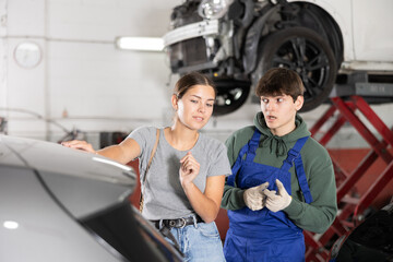 Interested female client talking to young auto mechanic, discussing needed maintenance of her car...