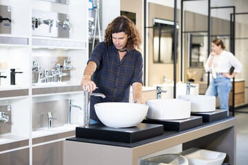 Male buyer compares several plumbing options on display.man chooses white ceramic sink....