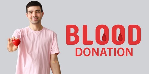 Young man with red heart on light background. Banner for World Blood Donor Day